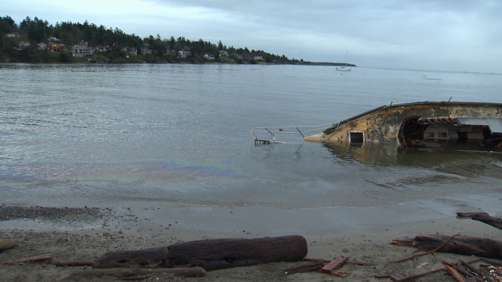 An oily sheen is seen in the water near an overturned derelict boat that washed ashore at Cadboro Bay, B.C., in December 2015. (CTV News)