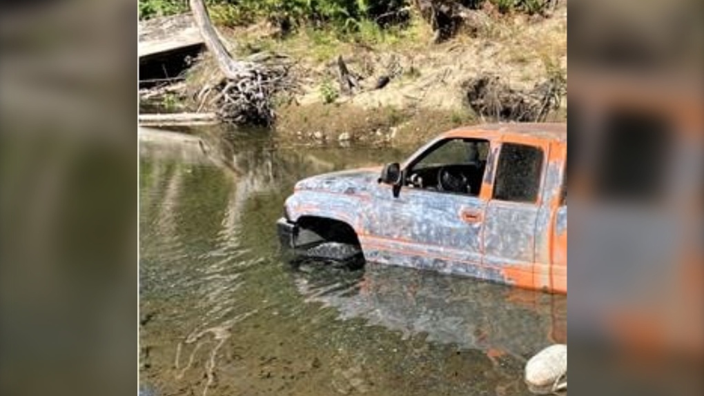 Photos shared with the post show a pickup truck with peeling orange paint submerged up to the top of its tires in the creek. (Facebook/BC Conservation Officer Service)